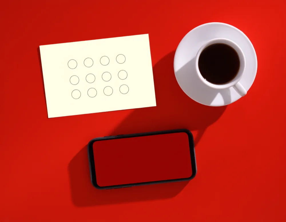 A blank paper stamp card, a phone with a plain red screen and a cup of coffee on the glossy red counter.