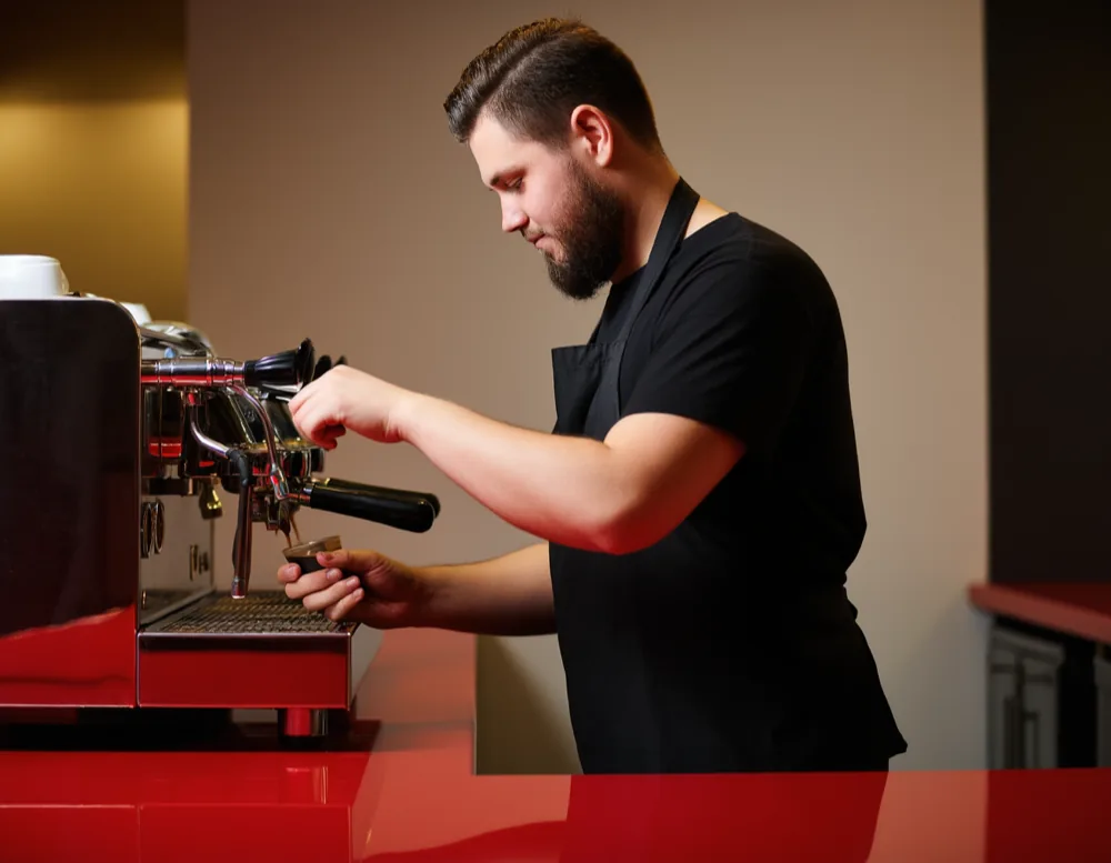 A barista in a black apron pulling a shot at the long red counter.